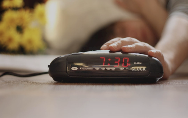 Hand hitting snooze on alarm clock